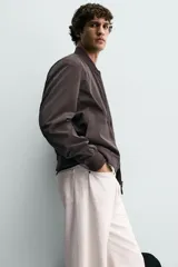 Cazadora bomber ligera de tejido técnico color verde oliva, con cuello, puños y bajo en rib elástico. Presenta cierre frontal de cremallera y bolsillos de vivo en la cadera.