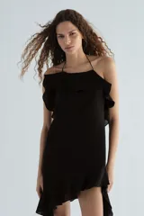Vestido corto negro con tiras halter finas, escote con volado amplio y bajo asimétrico con volado y cordón colgante.
