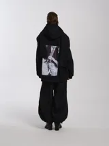 Buzo hoodie oversize de felpa de algodón color gris, con capucha y bufanda integrada que envuelve el cuello. Presenta cierre frontal y bolsillos canguro.