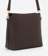 Cartera tipo hobo de tamaño pequeño, confeccionada en material sintético color marrón oscuro con acabado liso. Presenta una correa ajustable, cierre principal con cremallera y detalles metálicos dorados, incluyendo una placa con el logo de la marca en el frente.