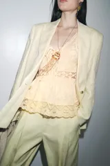 Top sin mangas color crudo, con escote en V y cierre frontal con lazos. Presenta bordados florales y detalles de encaje.