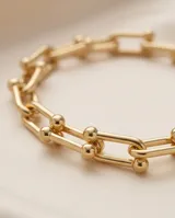 Pulsera de acero con baño de oro, compuesta por eslabones rectangulares unidos por esferas metálicas.