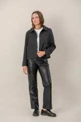 Chaqueta de paño color gris oscuro, con cuello camisero, cierre frontal de botones y dos bolsillos frontales tipo parche. Presenta un corte recto y mangas largas.