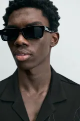 Camisa de corte relajado en color negro, confeccionada en tejido de algodón. Presenta cuello tipo bowling, manga corta y cierre frontal con botones. Cuenta con bordados lineales de hojas en la parte delantera.