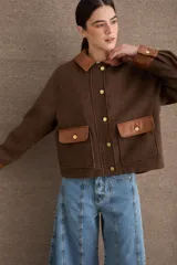 Campera corta de paño color marrón con detalles en cuero sintético al tono en cuello, puños y solapas de bolsillos. Presenta cierre frontal con botones metálicos dorados y dos bolsillos frontales tipo cargo.