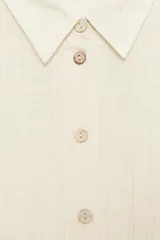 Camisa de cuello solapa y manga larga con sisa ancha, confeccionada en tejido con hilo metalizado y cierre frontal con botones.