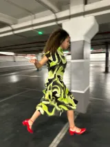 Vestido midi con estampado abstracto en tonos verde lima y negro, con cuello alto y volantes en la falda.