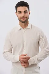 Camisa de lino a rayas finas en tonos beige y blanco, de manga larga con puños vueltos, cuello camisero y cierre frontal de botones. Cuenta con un pequeño logo bordado en el pecho.