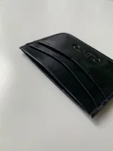 Tarjetero de cuero vacuno color negro con acabado brillante. Cuenta con cuatro ranuras para tarjetas y un bolsillo central.