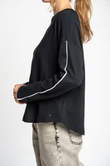 Sweater negro de calce oversize, confeccionado en algodón peinado con textura sutil. Presenta cuello redondo y una línea vertical blanca decorativa a lo largo de las mangas largas.