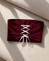 Top tipo strapless color bordó, con diseño cruzado de cordones blancos en la parte frontal y ojales metálicos.