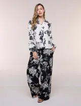 Conjunto de camisa y pantalón amplio con caída fluida. Camisa con escote en V y abotonadura frontal, mangas largas de corte caído con detalle de puntilla calada y puños elastizados fruncidos. Pantalón de tiro alto con cintura elastizada, pierna holgada de corte wide leg con dobladillo ancho en el ruedo y bolsillos laterales.