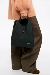 Bolso bandolera de estructura blanda marca Bimba y Lola, confeccionado en nylon con detalles en cuero. Presenta doble asa de mano, correa de tejido regulable y extraíble, cierre de cordón y logo metálico en el frente.