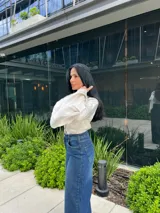 Blusa negra de manga larga con cuello camisero y puños acampanados o con aberturas.