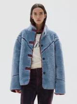 Campera de pelo sintético en color azul, con cuello alto y cierre frontal de botones. Presenta detalles de terminación en cuero vegano color bordó en los bordes, costuras y solapas.