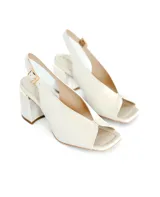 Zapato de tacón tipo sandalia destalonada en color off-white, confeccionado en cuero natural. Presenta un diseño con escote en el empeine, punta cuadrada y taco cuadrado de 7 cm con detalle metálico en la base.
