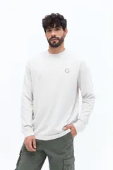 Remera de manga larga color blanco roto o gris muy claro, con escote redondo y un pequeño logo circular estampado en el pecho.