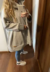 Canguro gris claro con cuello alto, mangas largas con puños en gris oscuro, bolsillo tipo canguro y corte holgado.