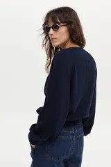 Sweater de tejido de punto color blanco marfil, con calce relajado, mangas largas levemente abullonadas, escote en V con botones y detalles de ribetes en color negro.