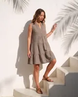 Vestido corto de lino natural color blanco, sin mangas, con cuello mao y escote en V con botones de nácar. Presenta diseño escalonado con volados fruncidos en la falda.