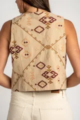Chaleco de algodón color beige con estampado geométrico en tonos bordó y marrón. Presenta escote en V, cierre frontal con botones y corte recto.