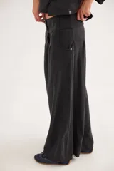 Pantalón de jean con diseño de tiro medio-bajo y piernas anchas. Presenta una pretina ancha con cierre de tres botones metálicos frontales, pinzas decorativas en la cintura y bolsillos delanteros funcionales.