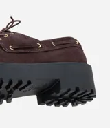 Mocasín estilo desert shoe confeccionado en cuero con acabado de gamuza color marrón oscuro. Presenta cordones frontales, detalles de ojalillos metálicos dorados y una suela flatform robusta de estilo track en color negro.