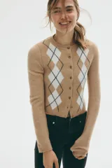 Saco corto de punto jacquard color beige, con estampado de rombos blancos y negros. Tiene cuello redondo, botonadura frontal y ribetes acanalados en puños y bajo.