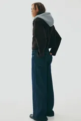 Campera negra de tejido suave efecto neopreno, con cuello y cierre frontal. Presenta un diseño de doble capa simulado con una capucha de tela gris claro que asoma por debajo del cuello de la campera.