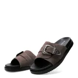 Sandalias chatas Miss Carol modelo Sage, color marrón, tipo slide con suela negra y una tira ancha en el empeine decorada con una gran hebilla metálica plateada de estilo western con grabados en relieve.