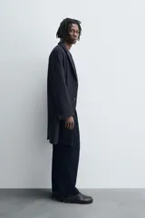 Abrigo de corte regular fit confeccionado en tejido compacto con mezcla de lana. Presenta cuello con solapas de muesca, cierre frontal de botonadura, bolsillos de vivo en la cadera y abertura central en la espalda.