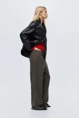 Pantalón de tiro alto en color marrón oscuro, con diseño de pierna recta y pliegues frontales cosidos. Presenta bolsillos de parche delanteros con botones decorativos dorados.