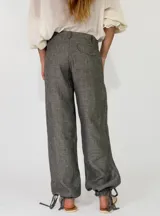Pantalón de lino color beige, de corte holgado tipo jogger con puños ajustables con cintas en los tobillos, bolsillos laterales y cierre frontal con botón y cremallera.