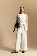 Pantalón ancho de tiro alto, color blanco roto con finas rayas verticales en color beige/marrón. Presenta un detalle de nudo o lazo en la cintura.