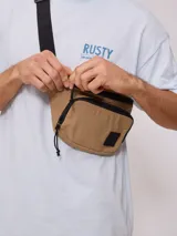 Riñonera de nylon color beige/camel, con acabado arrugado y detalles en negro, incluyendo cierres y tiradores de cordón. Posee un parche cuadrado negro con logo en el frente.