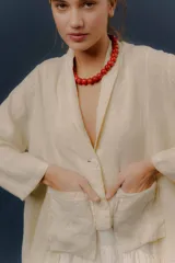Chaqueta de lino color beige, de calce relajado, con escote en V, cierre frontal con botones y bolsillos frontales aplicados.