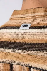 Camisa de manga corta con cuello solapa y cierre frontal de botones. Presenta un diseño de rayas verticales en tonos marrones, beige y negro, con una textura tejida y corte holgado.