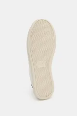 Zapatilla deportiva tipo bamba, color blanco, con suela plataforma engomada de color crema. Presenta pespuntes en el cuerpo y detalle en la talonera de color marrón oscuro.