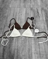 Corpiño de bikini tipo triángulo, con textura acanalada y tirantes regulables. Presenta un pequeño dije metálico en el centro.