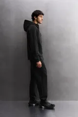 Sudadera con capucha y cierre de cremallera frontal, color negro, confeccionada en tejido técnico compacto de algodón elástico. Presenta cuello subido, bolsillos frontales con cremallera y acabado termofijado, y puños y bajo en rib del mismo tejido.