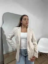 Blazer sastrero de corte clásico en color beige, con solapas tradicionales, cierre frontal de un botón y bolsillos laterales con solapa.