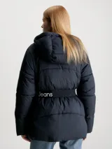 Campera puffer negra de nailon con capucha y cinturón con hebilla. Tiene cierre de cremallera y botón de presión, bolsillos en la cintura y logo monograma de Calvin Klein estampado en el pecho.
