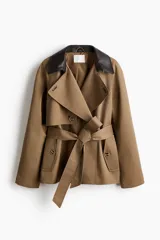 Gabardina corta de sarga color marrón claro, con doble botonadura, cuello de solapa en contraste de color negro con efecto cuero, bolsillos laterales con solapa y cinturón ajustable para anudar en la cintura.