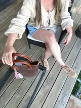 Bolso matera de cuero color marrón con doble asa de mano y correa larga desmontable. Incluye accesorio decorativo de borlas rosas y blancas.