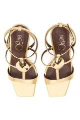 Sandalias de tacón alto PatBo modelo Zulu, color dorado metalizado, con tira en la puntera, diseño en T con aplique rígido en forma de concha marina, correa ajustable al tobillo y plantilla marrón.