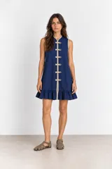 Vestido corto azul marino sin mangas, con cuello mao y cierre frontal de alamares decorativos en tono beige. Presenta ribetes en contraste y un delicado volado en el ruedo.