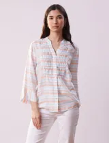 Blusa estampada a rayas horizontales en tonos celeste, blanco y naranja, con cuello mao, escote en V y abertura con botones. Delantero con punto smock. Manga ¾ con terminación amplia.