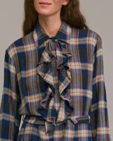 Vestido largo camisero con estampado a cuadros en tonos azul, marrón y beige. Presenta cuello camisero con volantes y mangas largas. Incluye cinturón de la misma tela para ajustar a la cintura.