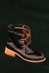 Botas de cuero negro de caña corta con cordones y costuras artesanales en hilo marrón claro, suela de madera con taco bajo y detalle de corderito en el borde superior.