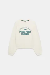 Sudadera color crema con cuello redondo, manga larga y estampado frontal en verde oscuro con el texto "Mountain Air Forever 1985 PIKES PEAK COLORADO".